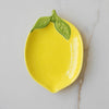 Yellow ceramic lemon-shaped dish with green leaf on a marble surface