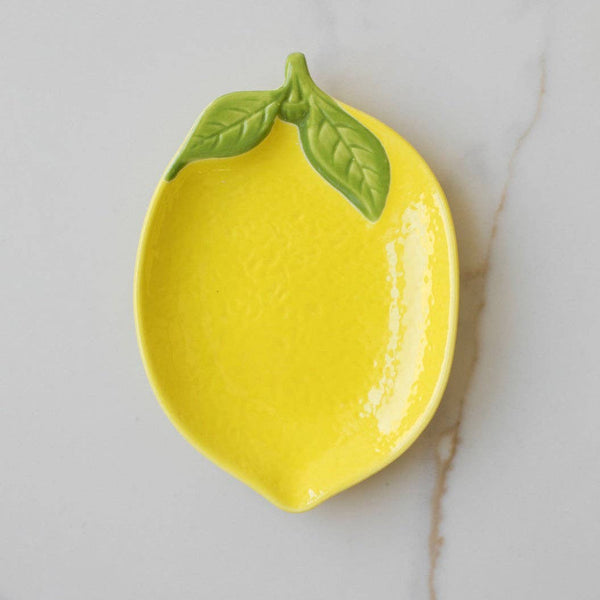 Yellow ceramic lemon-shaped dish with green leaf on a marble surface