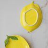 Two yellow ceramic lemon-shaped plates on a marble surface, one laid upside down showing the base. 
