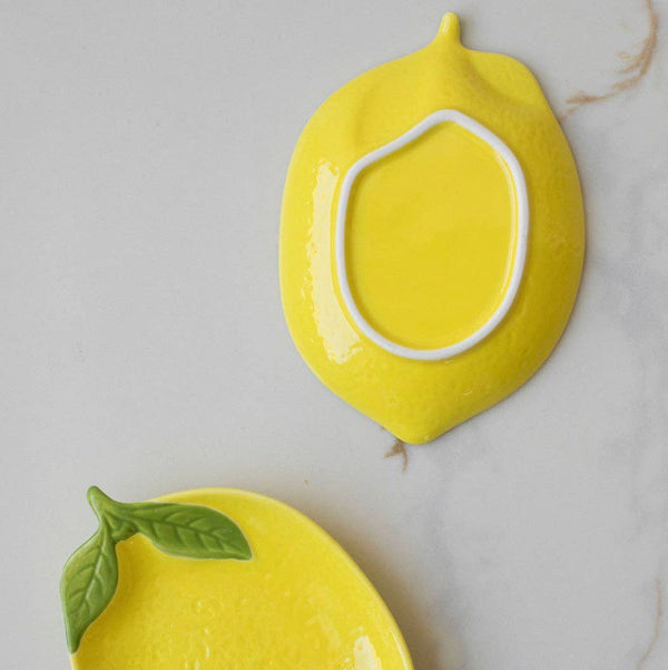 Two yellow ceramic lemon-shaped plates on a marble surface, one laid upside down showing the base. 