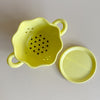 Top-down view of a yellow ceramic berry bowl colander and matching drip plate on a neutral background