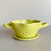 Yellow ceramic colander bowl with drip plate on a neutral background