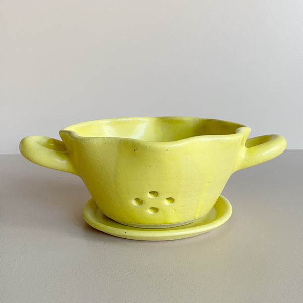 Yellow ceramic colander bowl with drip plate on a neutral background