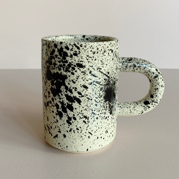 Off-white and black speckled ceramic mug on a plain background