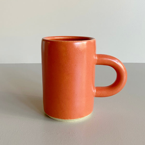 Red-orange ceramic mug with arched handle on a neutral background