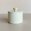 Soft white ceramic salt cellar with a wooden handle on a neutral background