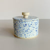 Speckled blue and white ceramic salt cellar with a wooden handle on a neutral background