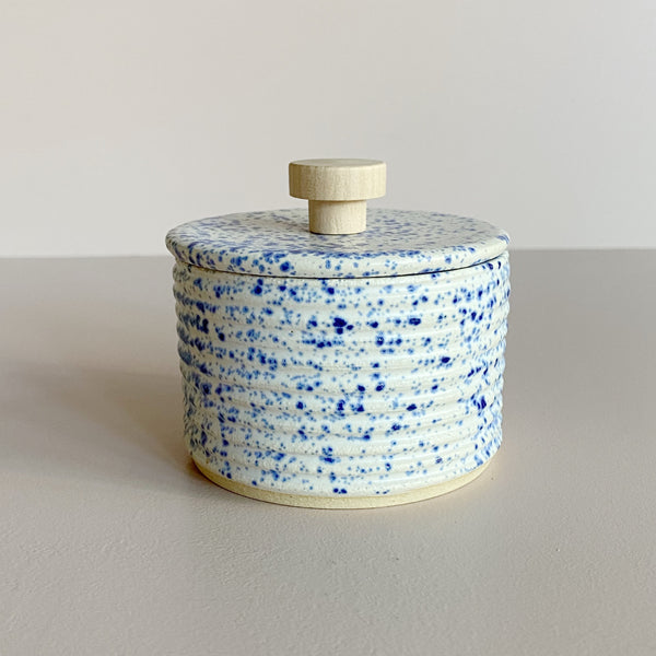 Speckled blue and white ceramic salt cellar with a wooden handle on a neutral background