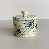 Black speckled ceramic salt cellar with wooden handle on a plain background