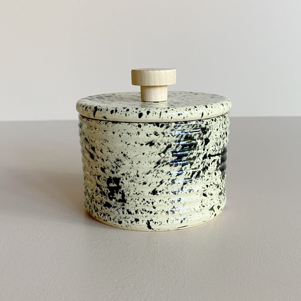 Black speckled ceramic salt cellar with wooden handle on a plain background