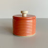 Bold red-orange ceramic salt cellar with a wooden handle on a neutral background
