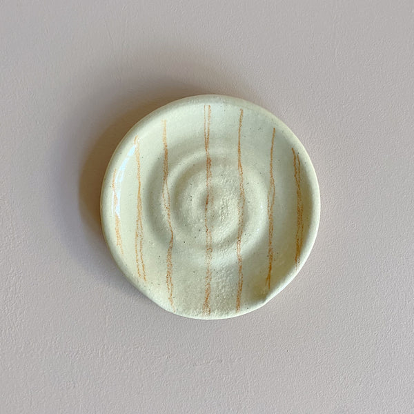 Round ceramic spoon rest with rust orange stripes on a neutral background