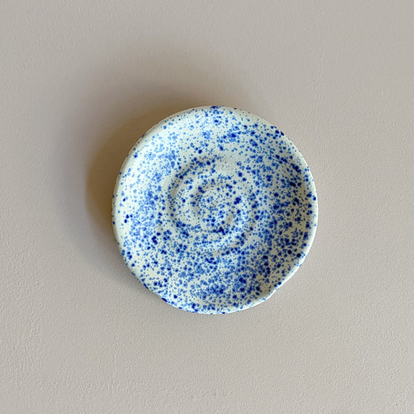 Small ceramic spoon rest with blue speckles on a neutral background