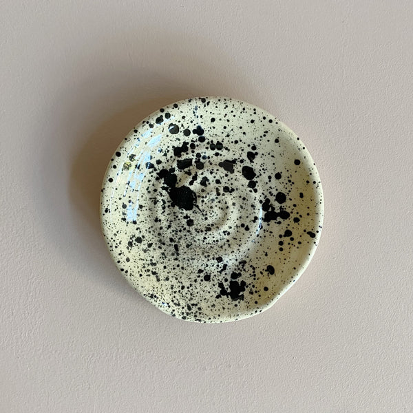 A ceramic spoon rest with a black speckled pattern on a neutral background.
