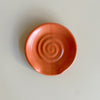 A vibrant red-orange ceramic spoon rest on a neutral background.