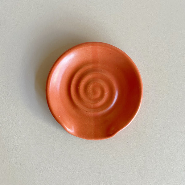 A vibrant red-orange ceramic spoon rest on a neutral background.