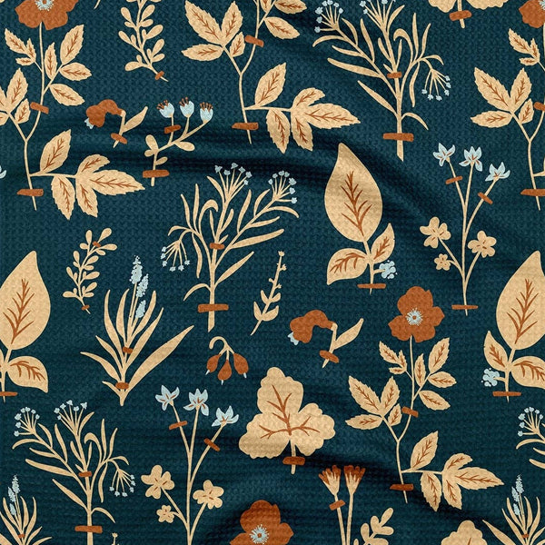 A detailed view of a kitchen towel in navy with a botanical print in tan, orange, and light blue.