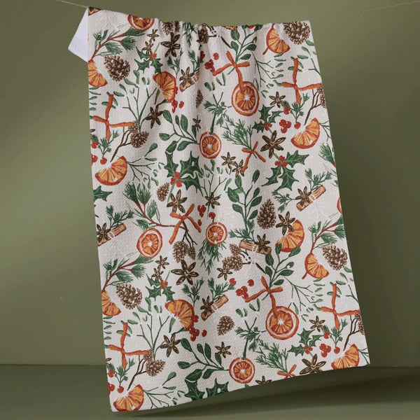 A tea towel in white with orange, green, and brown botanical designs hanging from a wire against a green wall.