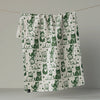 A white kitchen towel printed with a green pattern of cats, hanging from a thin string against a neutral gray background and revealing the reverse side, which has a print of tiny stars.