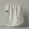 A white kitchen towel with a green star pattern, hanging from a string against a neutral gray background, revealing a bit of the reverse side with a cat print.