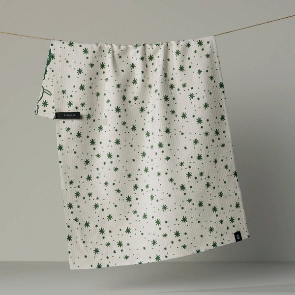 A white kitchen towel with a green star pattern, hanging from a string against a neutral gray background, revealing a bit of the reverse side with a cat print.