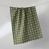 An olive green and white patterned tea towel hangs from a wire against a soft white background.