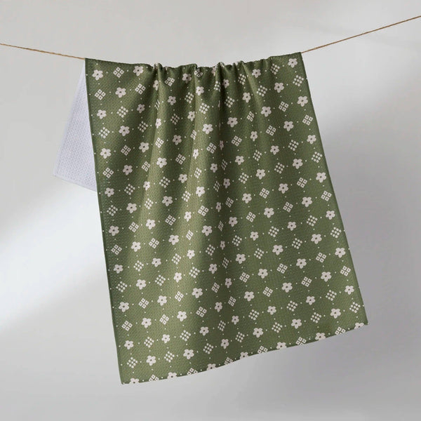 An olive green and white patterned tea towel hangs from a wire against a soft white background.
