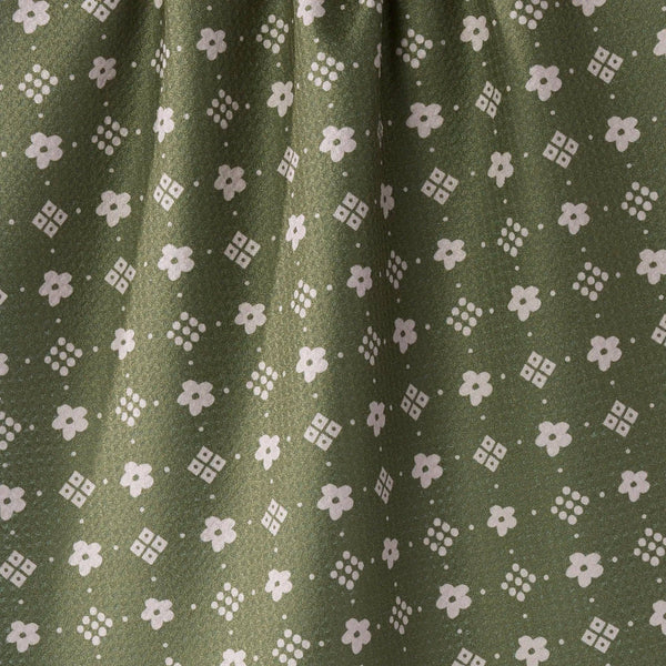 Close-up of olive green tea towel with a repeating white floral and geometric pattern.