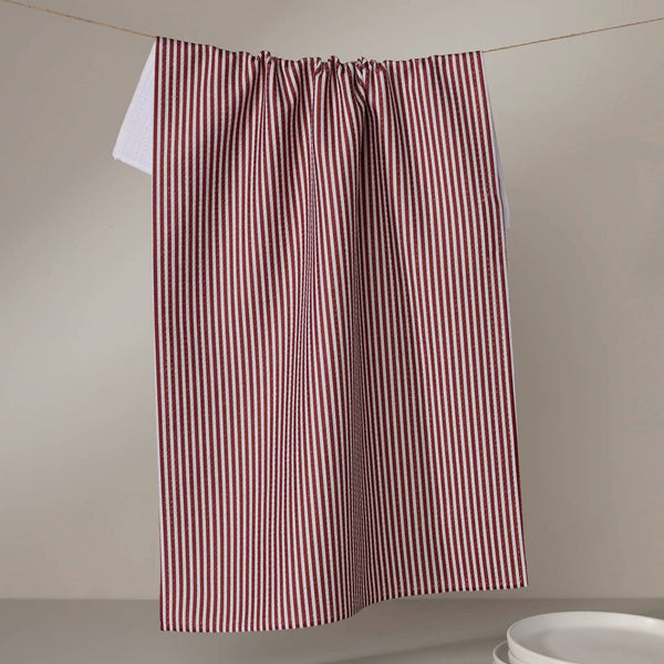 Red and white striped tea towel hanging on a line against a beige wall with white plates at the bottom.