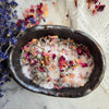 Bath salts with dried flowers in a black dish on a marble surface