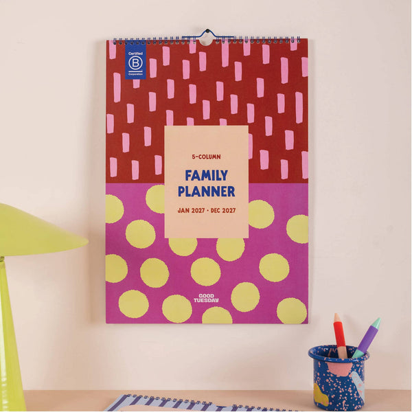 Family planner for 2027 with colorful design on a wall, next to a cup with pens.