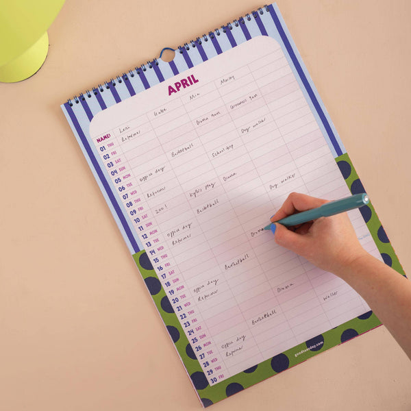 Person writing in a colorful monthly planner for the month of April on a beige surface