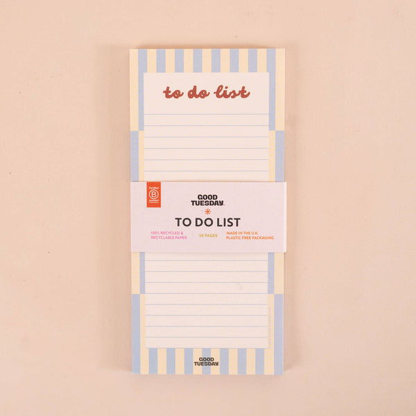 A vertical to-do list notepad with a white paper band around the middle, featuring pastel blue and cream stripes and the words 'to do list' at the top, photographed on a solid beige background.
