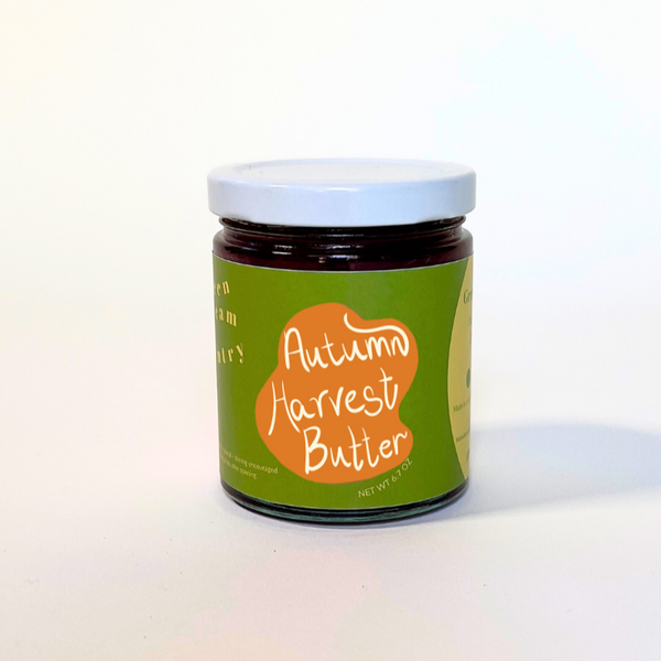A small glass jar of autumn harvest butter with a green and orange label, set against a plain white background.
