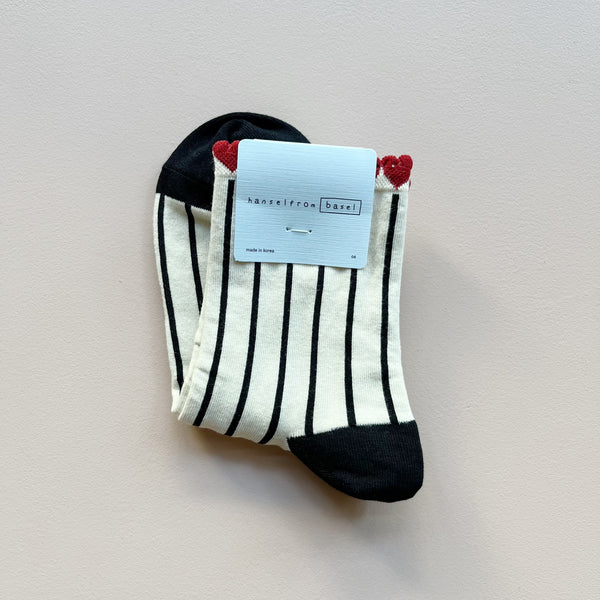 A pair of short crew socks with 'hansel from basel' packaging featuring a white and black stripe pattern and a top trim of red "tulip" hearts, laying against a neutral background.