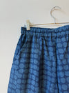 Blue patterned pants hanging on a hanger against a light background