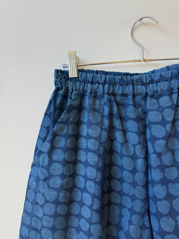 Blue patterned pants hanging on a hanger against a light background