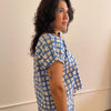 Woman wearing a blue and white patterned top against a plain wall.