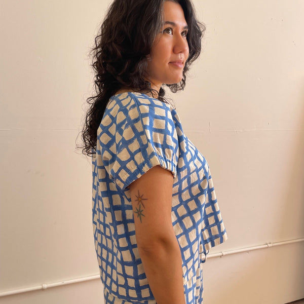 Woman wearing a blue and white patterned top against a plain wall.
