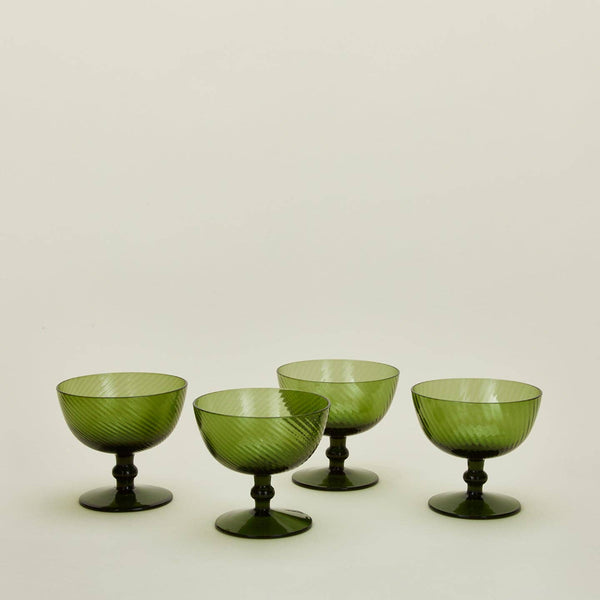 Four green glass coupe-shaped cups with ribbed details and pedestal bases, arranged on a plain light background.