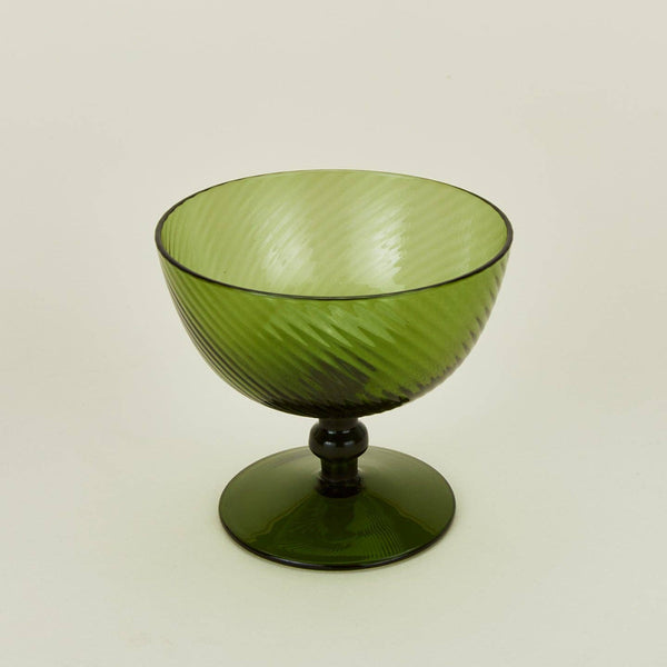 An olive green coupe glass with a ribbed, swirled texture, featuring a flared bowl and a short pedestal base, set against a plain off-white background.