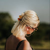 A woman with blonde hair standing outside facing away from the camera. Her hair is half up, decorated with a stack of three wildflower mini hair claws.