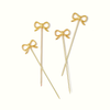 Four gold bow-shaped cocktail picks on a solid white background.