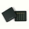 Four gold bow-shaped cocktail picks displayed in a dark gift box next to its matching lid, which is printed with the brand name 'HOUSE OF GLEASON'.