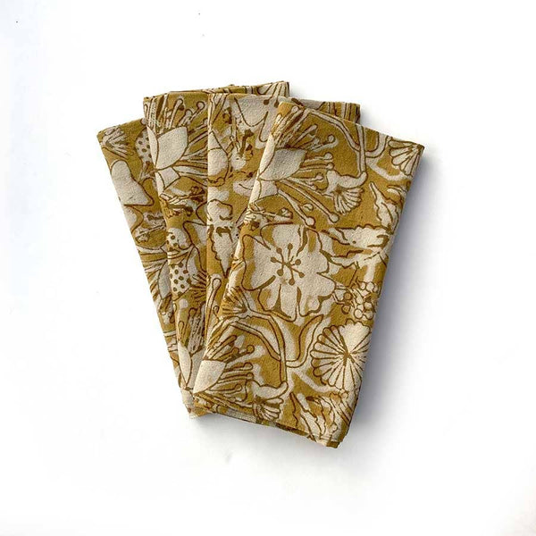 A stack of four folded cotton napkins in a rich golden yellow and off-white floral design against a white backdrop.