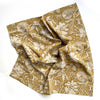 A rich ochre yellow and off-white floral print cotton napkin scrunched up against a white backdrop.