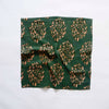 A dark green and warm orange-brown patterned cotton napkin scrunched up on a white backdrop.