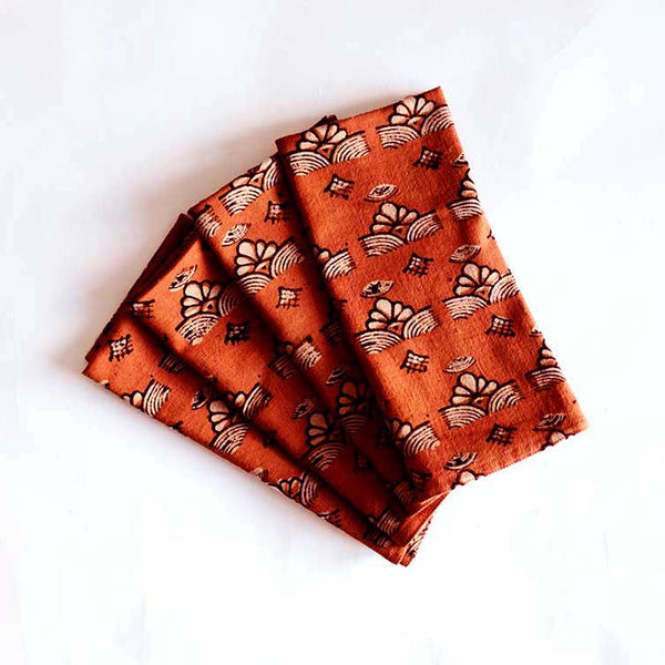 A stack of four fabric napkins in a rich orange shade with off-white and black patterns against a white backdrop.