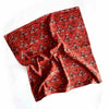 A rich red-orange cotton napkin sporting an off-white and black block print design on a white backdrop.