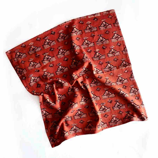 A rich red-orange cotton napkin sporting an off-white and black block print design on a white backdrop.